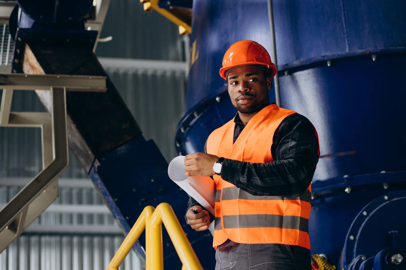 An engineer wearing orange protective equipment beside a processing vessel