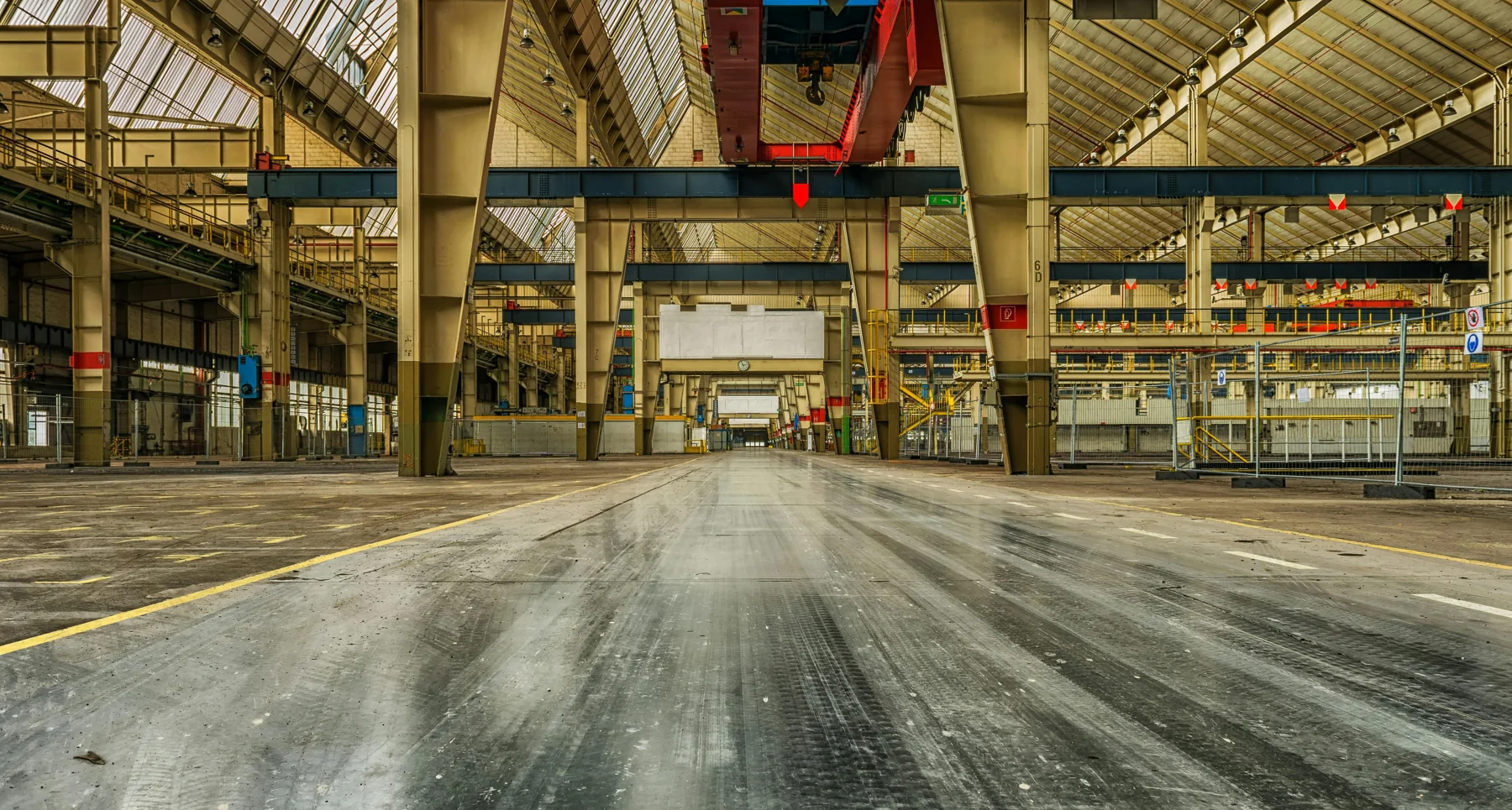 A wide industrial workshop with overhead cranes and marked equipment routes
